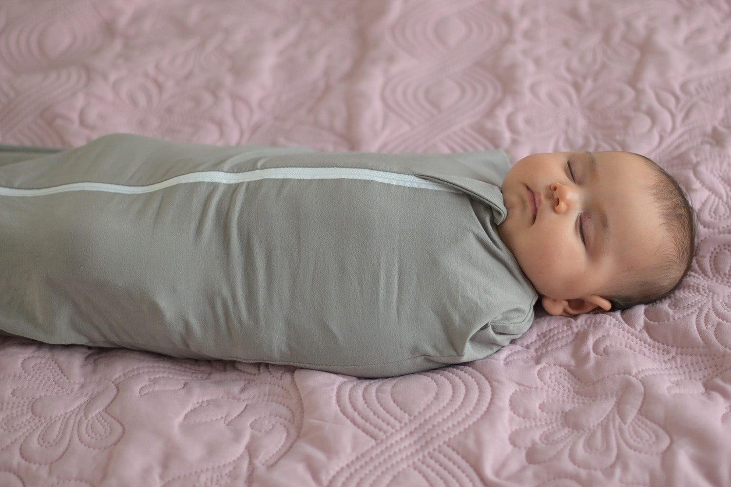 Baby sleeping in a grey calm swaddle on a pink blanket