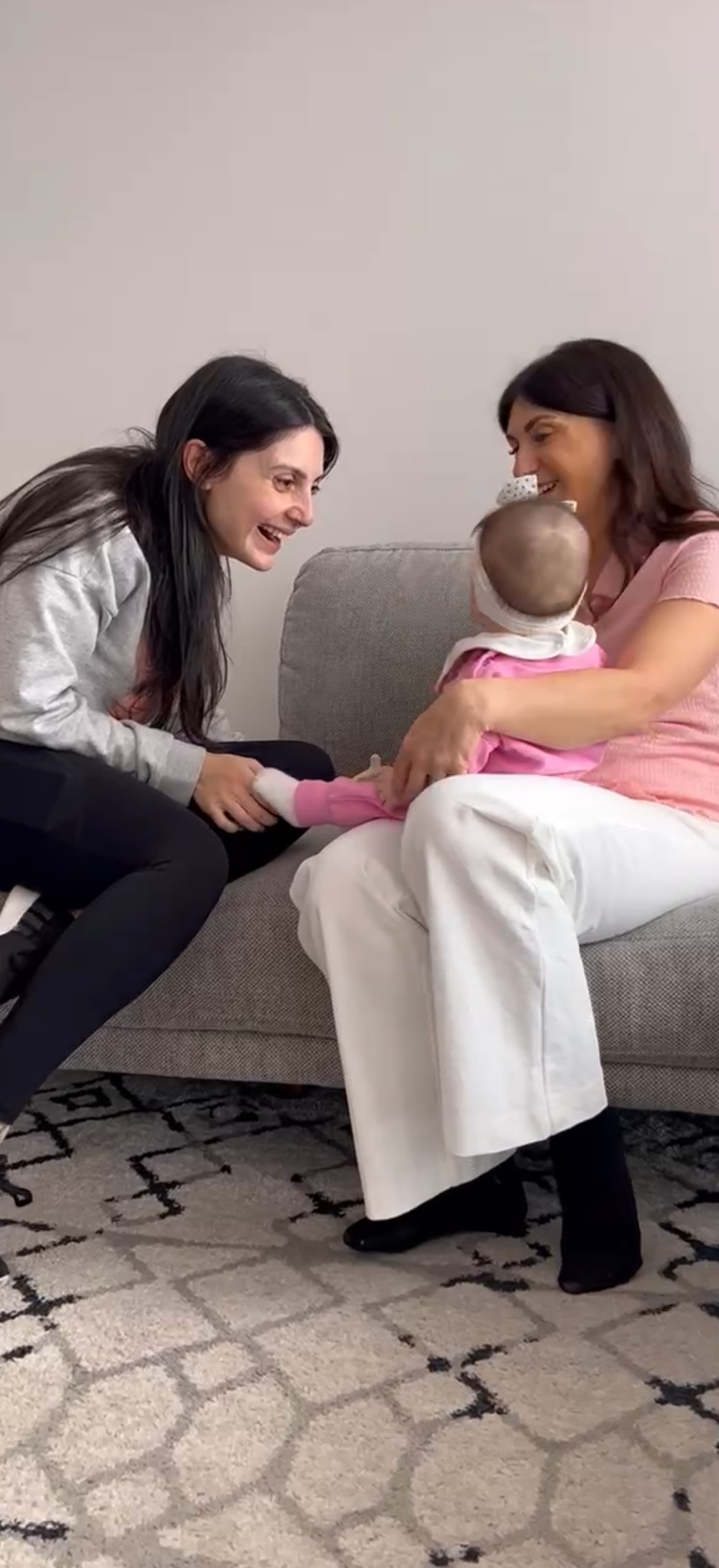 Two women sitting on a couch with a baby, smiling and interacting.