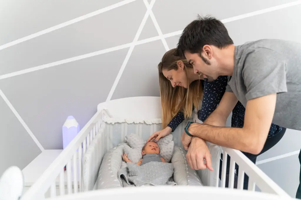 A couple of parents looking their newborn baby in the cradle- sleep consultant